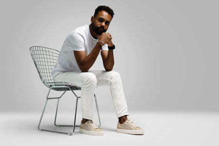 Handsome young african american guy sitting on stool, posing in studio - isolated.の写真素材