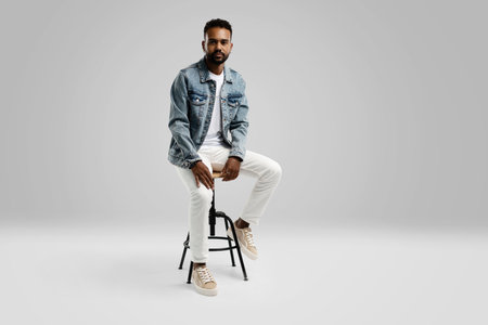 Handsome young african american guy sitting on stool, posing in studio - isolated.の写真素材