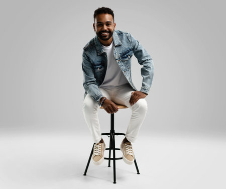 Handsome young african american guy sitting on stool, posing in studio - isolated.の写真素材