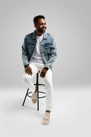 Handsome young african american guy sitting on stool, posing in studio - isolated.の写真素材