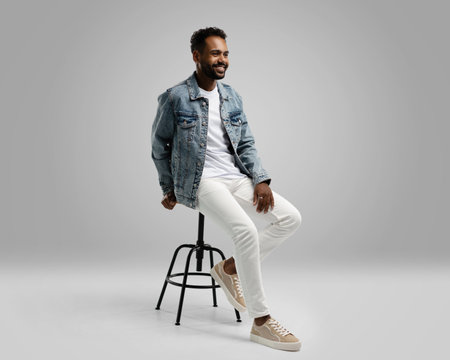 Handsome young african american guy sitting on stool, posing in studio - isolated.の写真素材