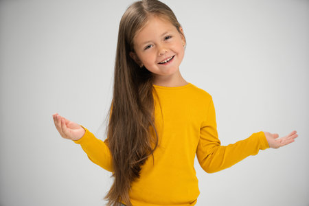 Adorable six years old girl isolated on white studio background, pretty brown-haired fringe hairstyle european appearance child pose indoor smiling look at camera, generation Z conceptの写真素材