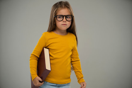 Serios little kid girl 5-6 years old isolated on white background, children studio portrait. Childhood lifestyle concept. Mock up copy space. Holding bookの写真素材
