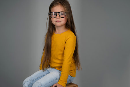 Portrait of little girl in sweatshirt and jeans sitting on box in studio against white backgroundの写真素材