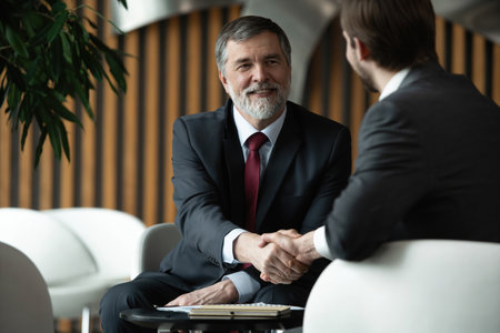 Business partnership meeting in office. Mature businessman shake hands with a younger colleagueの写真素材