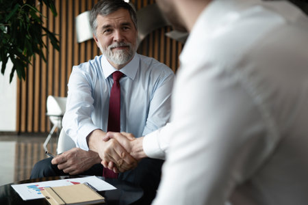 Business partnership meeting in office. Mature businessman shake hands with a younger colleagueの写真素材
