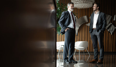 Two businessmen deep in discussion together while standing in modern officeの写真素材