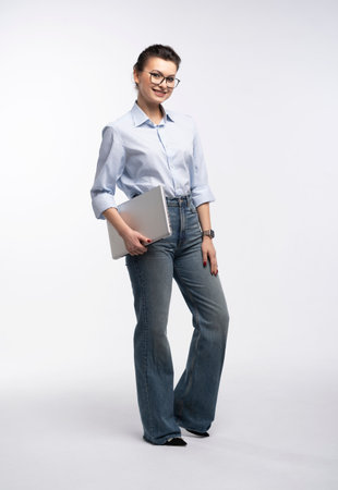 Full length of portrait of a smiling businesswoman carrying laptop computer standing isolated over white backgroundの写真素材