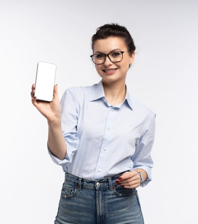 Business woman pointing at a blank smartphone screen for advertisement or mockup purposes, showcasing professionalism and innovation, isolated on white backgroundの写真素材