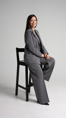 Portrait of a cheerful young businesswoman sitting in a chair against white background. Full bodyの写真素材
