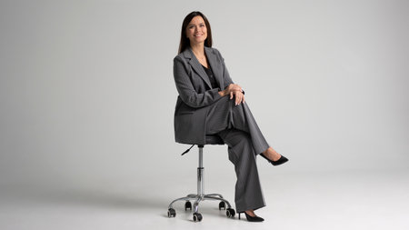 Portrait of a cheerful young businesswoman sitting in a chair against white background. Full bodyの写真素材