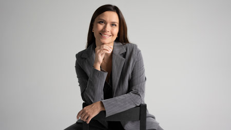 Portrait of a cheerful young businesswoman sitting in a chair against white backgroundの写真素材