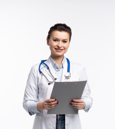 Portrait of friendly woman doctor in uniform holding clipboard, smiling at camera, cheerful female therapist with stethoscope posing on white backgroundの写真素材