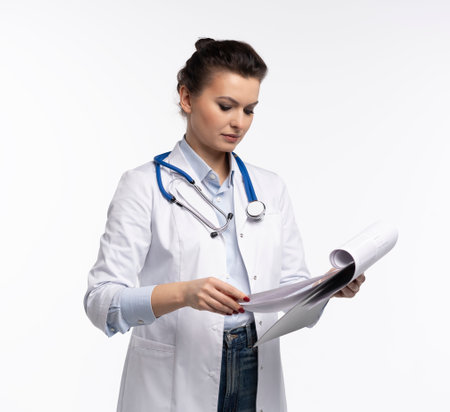 Portrait of friendly woman doctor in uniform holding clipboard, smiling at camera, cheerful female therapist with stethoscope posing on white backgroundの写真素材