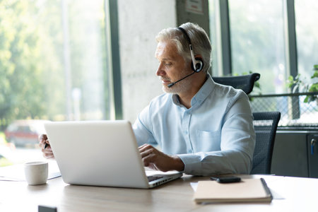 Smiling businessman using headset when talking to customer. Tech support manager in headset...