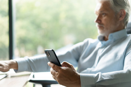 Mature 45 years old business man executive, business owner or entrepreneur sitting at desk using mobile cell phoneの写真素材