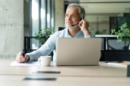 Smiling businessman using headset when talking to customer. Tech support manager in headset...