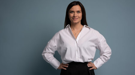 Beautiful, attractive, middle aged woman wearing casual white shirt standing isolated on blue background. Confident successful female looking at camera. Business conceptの写真素材