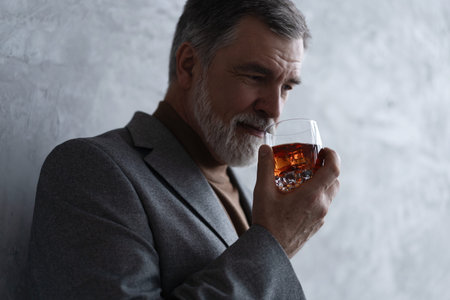 Confident mature businessman chilling relaxing drinking enjoying whiskey against grey wall
