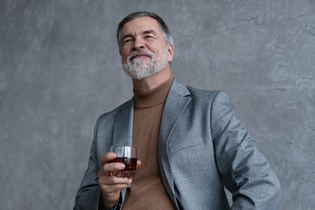 Confident mature businessman chilling relaxing drinking enjoying whiskey against grey wall