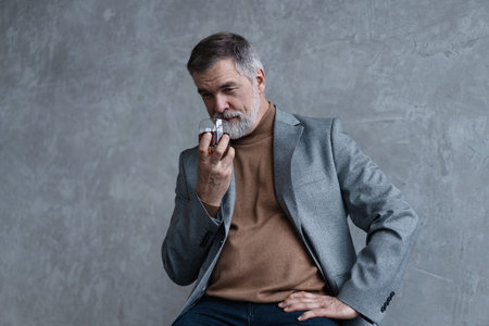 Confident mature businessman chilling relaxing drinking enjoying whiskey against grey wall