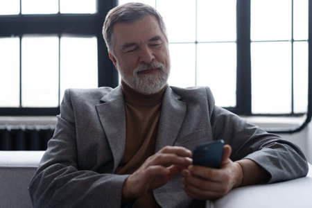 Mature smiling man using smartphone while sitting on sofa