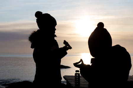 Silhouettes of Kids Eating Packed Lunch Outdoorsの写真素材