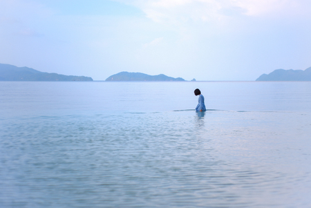 The girl is lonely in the sea with mountains in background.のeditorial素材