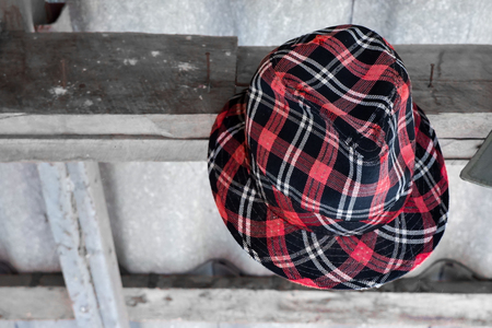 Red plaid hat hangs on nails on wooden wall.の写真素材