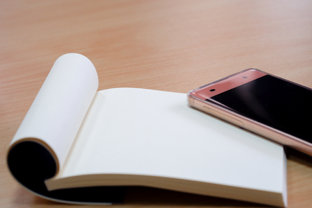 Pink mobile and notebook placed on a wooden desk.の写真素材