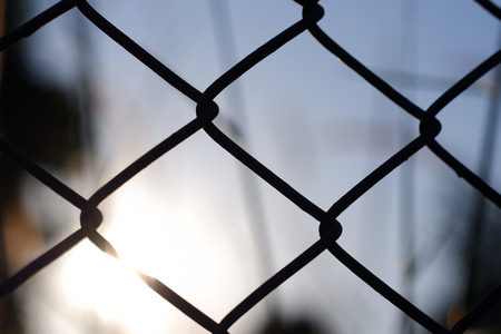Chain link fence and a sunrise with nature blurred background. Wire fence or metal net at sunset.の写真素材