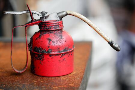 Old red oil spray container or oil can with oil stains placed on a wooden table.の写真素材