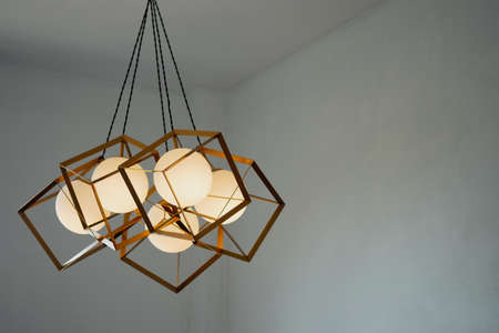 A round lamp with a rectangular iron frame suspended from the ceiling, illuminating in gold....