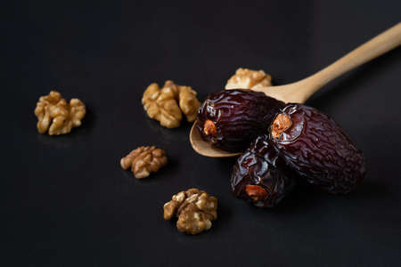 Med jool dates fruits in wooden spoon and walnuts on black background.の写真素材