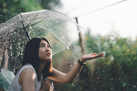 Asian woman spreads an umbrella and reaches out to play in the rain with a happy smile. Single life concept.の写真素材