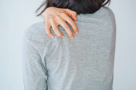 A woman scratching her back through her shirt. Skin disease concept.の写真素材
