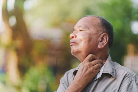 Side view of an old man with sore throat due to flu or COVID-19 symptoms. Concept of sickness of the elderly.の写真素材