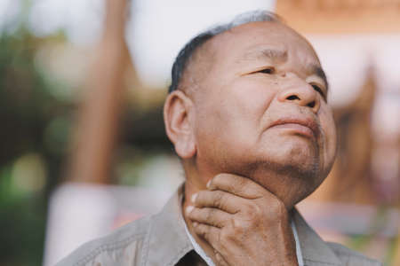Close-up of an elderly man has a sore throat due to flu or COVID-19. Concept of sickness of the elderly.の写真素材