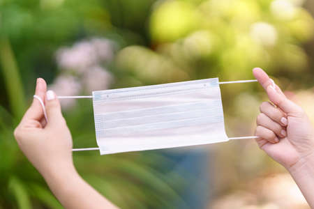 Woman's hand holding a mask with two hands with blurred nature background. Concept of disease...