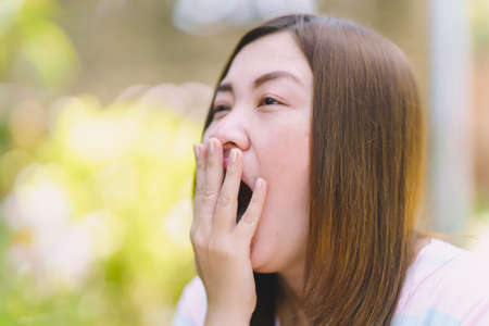 Thai woman covering her mouth while yawning.の写真素材