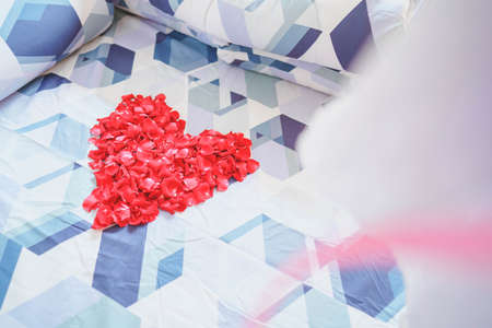 Red rose petals arranged in a heart shape on a couple's bed.の写真素材