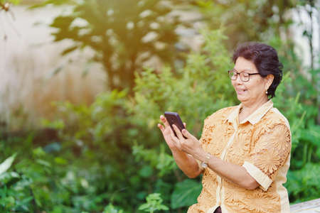 An elderly Thai woman is using a smartphone for shopping or texting with a smiling face.の写真素材