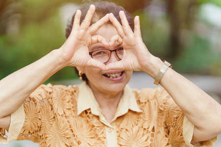 The old woman is smiling and making heart-shaped hands. The concept of happy living for the elderly.の写真素材