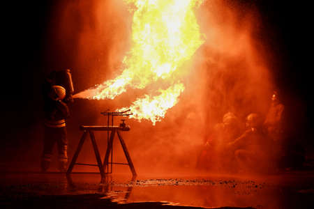 A team of firefighters is practicing to extinguish a blazing fire at night.の写真素材