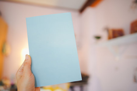 Hand holding a blue book with a blank cover for putting text in the room.の写真素材