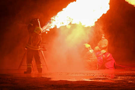A team of firefighters is practicing to extinguish a blazing fire at night.