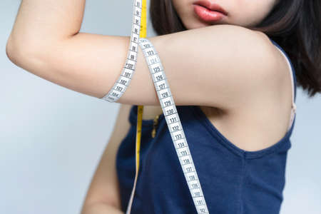 A woman measuring the proportions of her upper arm with a tape measure after exercise. Beauty or health concept.の写真素材
