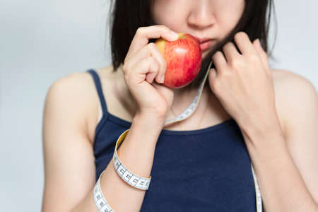 Woman holding red apple and measuring tape on her mouth, Beauty or health concept.