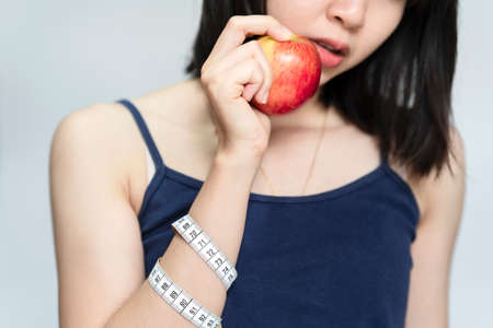 Woman holding red apple and measuring tape on her mouth, Beauty or health concept.の写真素材