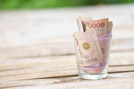 Thai banknotes in glass and wallet placed on a wooden table. Business and Finance Concepts. Copy...